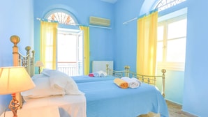 Un dormitorio con cubrecama azul, una mesita de noche blanca con lámpara y cortinas amarillas.