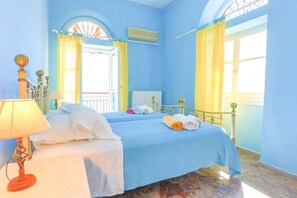 Ein Schlafzimmer mit blauer Bettdecke, einem weißen Nachttisch mit Lampe und gelben Vorhängen.
