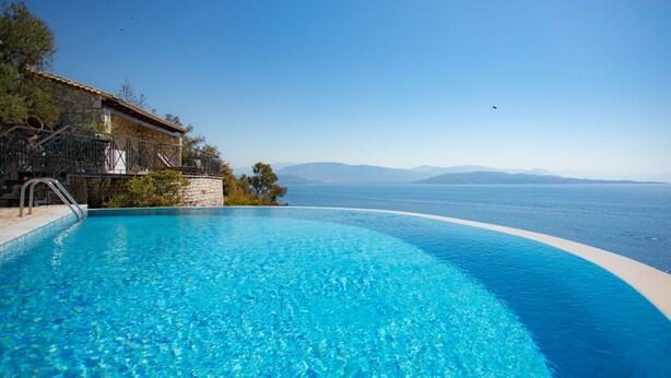 Una piscina infinita de agua cristalina con un edificio de piedra y vistas al mar y a las montañas.