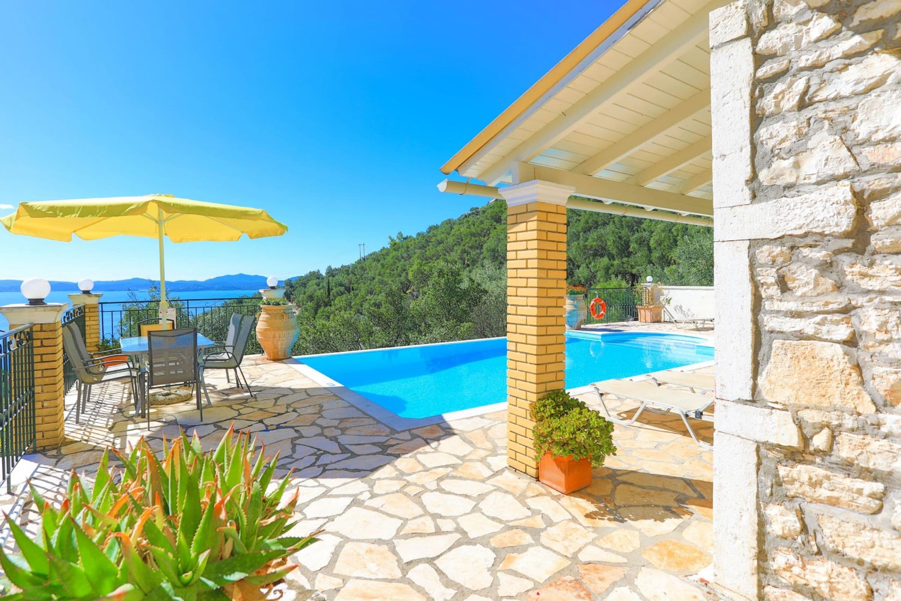 Un área de piscina con patio de piedra, una sombrilla amarilla y vistas a las montañas.
