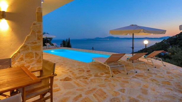 Un espacio al aire libre con suelo de piedra, piscina, sillones de descanso y sombrillas.