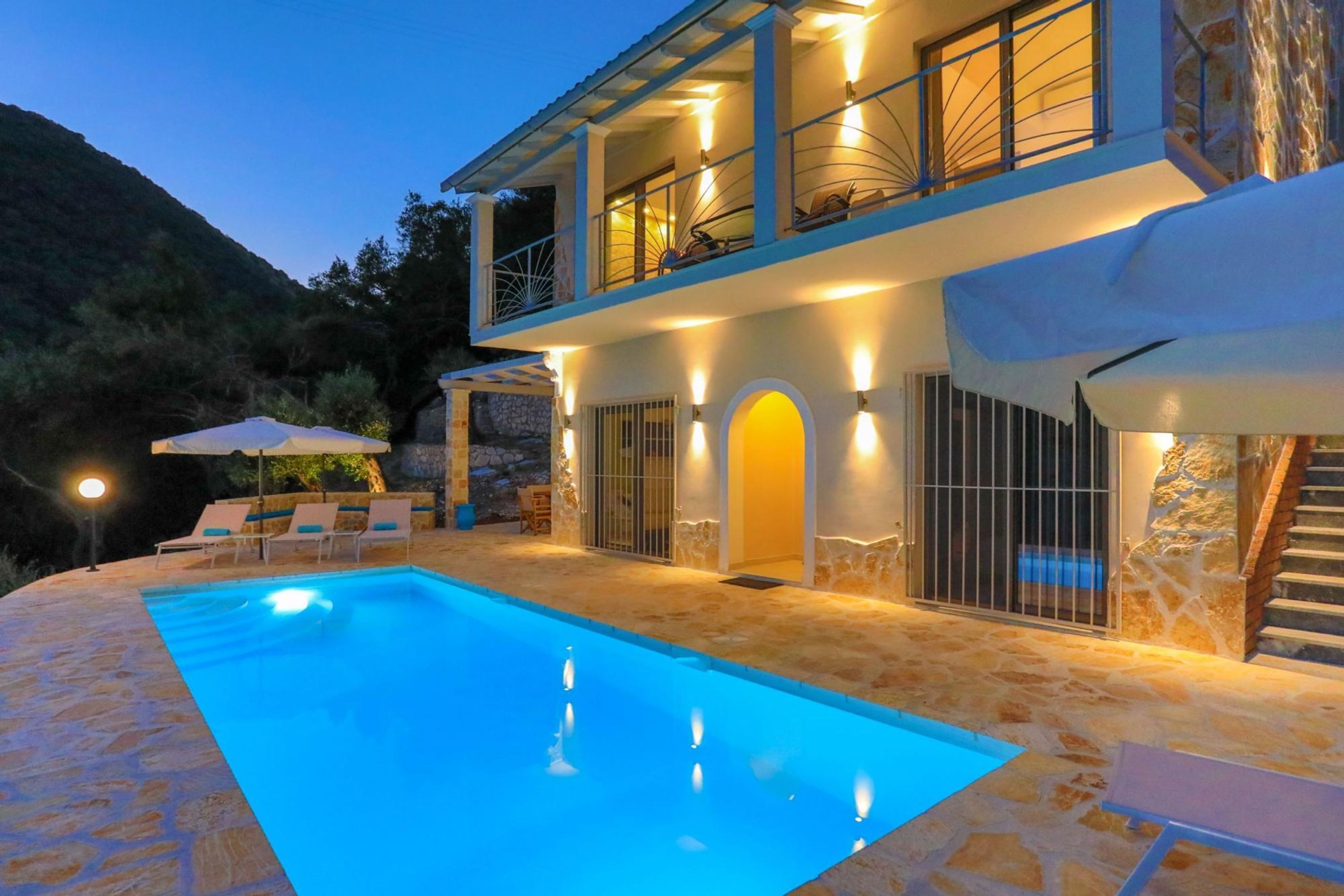 A two-story house with a swimming pool, stone walls, and outdoor seating.