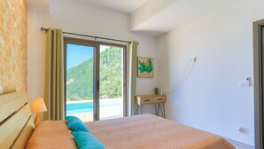 Un dormitorio con cama, mesita de noche, lámpara, un cuadro y vista al exterior.