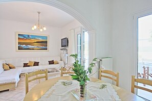 A well-lit room with a dining table, chairs, a sofa, a TV, and a painting on the wall. - Villa Oneiro in Apraos (Apraos)