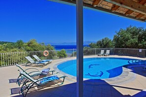 A swimming pool with a view of the sea, surrounded by lounge chairs and a safety sign. - Villa Oneiro in Apraos (Apraos)
