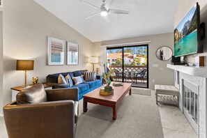 A living room with a blue sofa, a wooden coffee table, a leather armchair, a ceiling fan, and a fireplace. - Spacious 2 Bed 2 Bath Condo with Gourmet Kitchen in Carmel Valley for Long Term Stays (San Diego)