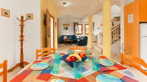 Een eetruimte met een tafel voor vier personen, een houten kapstok en een woonkamer op de achtergrond.