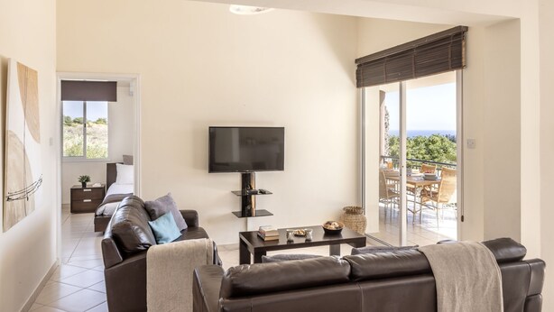 En moderne stue med et fladskærms-tv, lædersofaer, et sofabord og en balkon med udsigt.