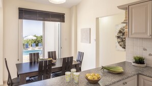Et køkken med en bordplade i granit, et spiseområde med et bord og stole, udsigt til en pool udenfor og en potteplante på disken.