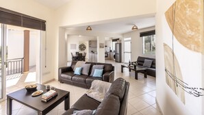 En rummelig opholdsstue med sofa, sofabord og spisebord. Et køkken i baggrunden med moderne hårde hvidevarer.