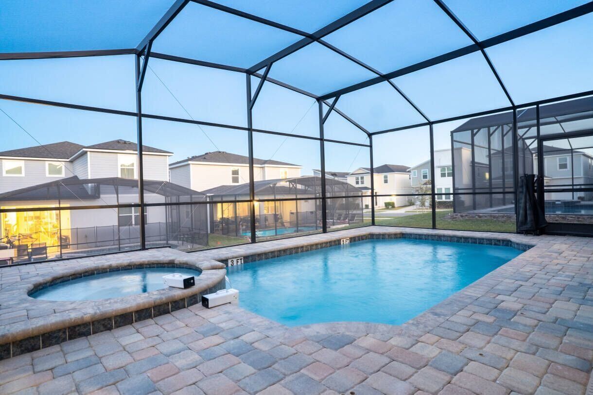 A swimming pool with a hot tub, surrounded by a glass enclosure with a view of neighboring houses.