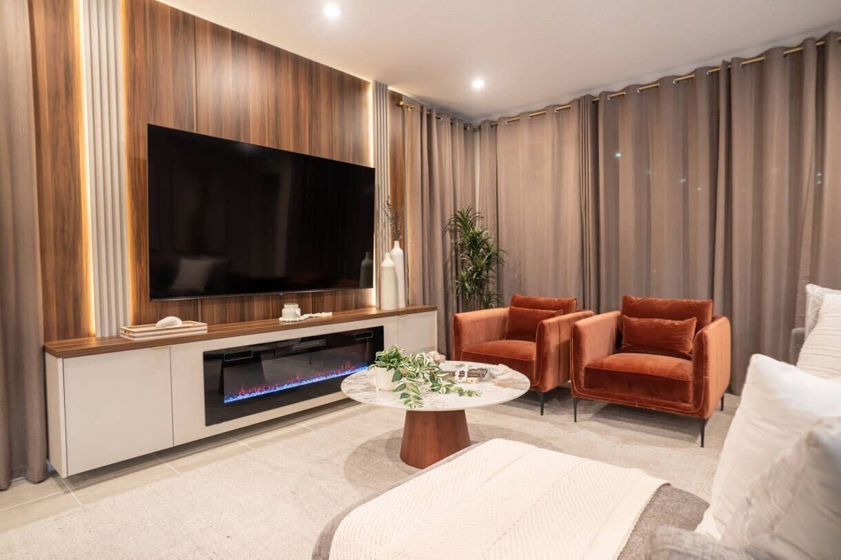 Ein modernes Wohnzimmer mit Flachbildfernseher, zwei Sesseln, einem Couchtisch und einem Kamin.