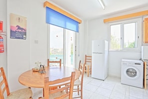 A kitchen with a washing machine, a refrigerator, and a dining area with a table and chairs. - Villa Aphrodite Finiki (Latchi)