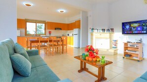 Un soggiorno moderno con un divano, un tavolino da caffè con della frutta, una televisione e una cucina sullo sfondo.