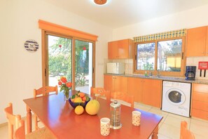 A kitchen with wooden cabinets, a washing machine, and a dining table with chairs. - Villa Athina Finiki in Latchi (Latchi)
