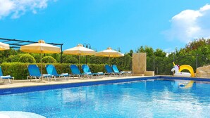 Une piscine entourée de verdure, avec des chaises longues bleues et des parasols jaunes.