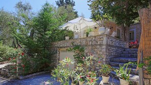 A stone building with a white umbrella, surrounded by potted plants and trees. - Lili Luxury Cottage in Ozias (Ozias)
