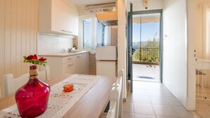 A modern kitchen with white cabinets, a wooden table, and a red vase with flowers. - Antigoni Villa Ena in Longos (Longos)