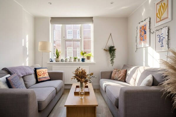 A modern living room with two sofas, a coffee table, and a window with plants. - [Superhost] 12 mins walk to Buckingham Palace & Big Ben - Cozy 2BR Family Rental (London)