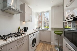 A compact kitchen with a gas stove, washing machine, and modern appliances. - [Superhost] 12 mins walk to Buckingham Palace & Big Ben - Cozy 2BR Family Rental (London)
