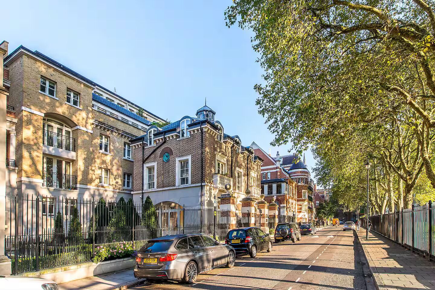 Een straat met aan weerszijden traditionele bakstenen gebouwen, geparkeerde auto's en een trottoir met bomen.
