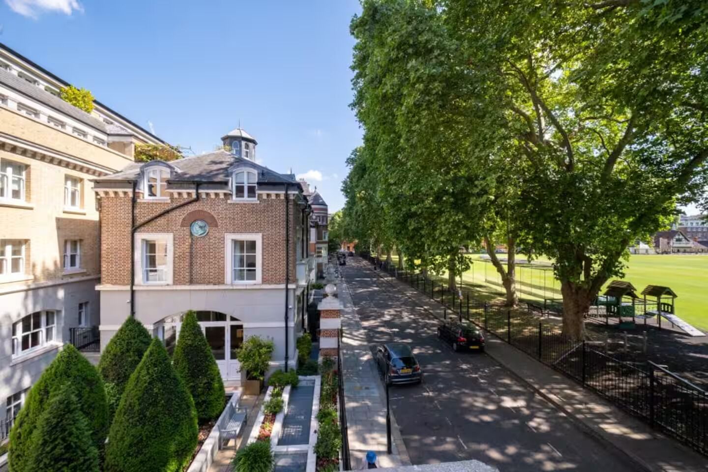 Straßenansicht mit einer Reihe von Ziegelgebäuden, einem Baumschattenspazierweg und einem Spielplatz.