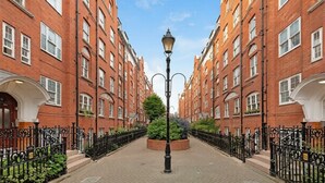 En gata med byggnader i rött tegel, en central gatlykta och en rund plantering med grönska.