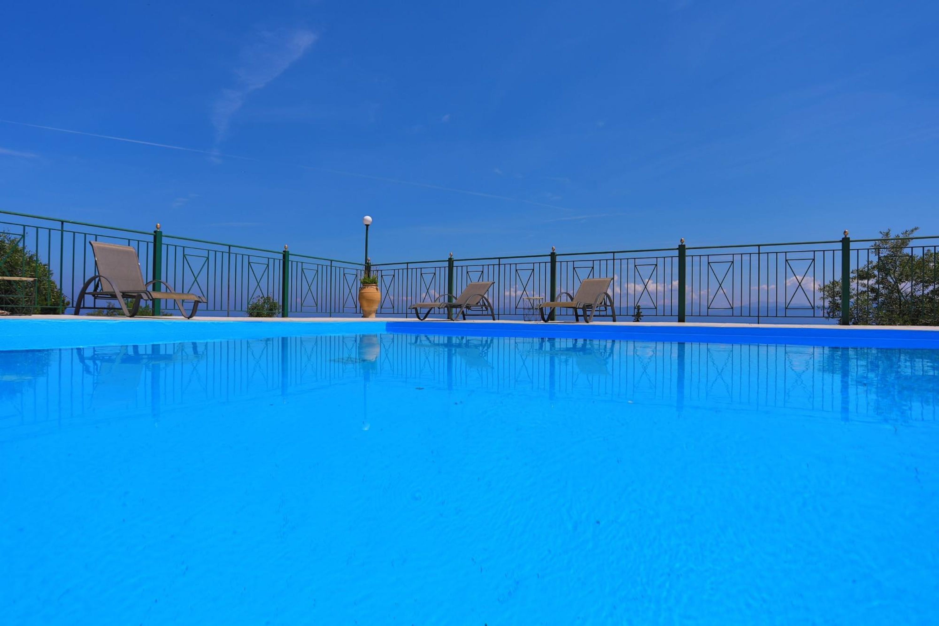 Une piscine dotée d’une plage bleue, entourée d’une clôture verte et de chaises longues.