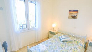 A bedroom with a bed, a nightstand, a lamp, a window with curtains, and a painting on the wall. - Antigoni Villa Tria in Longos (Longos)