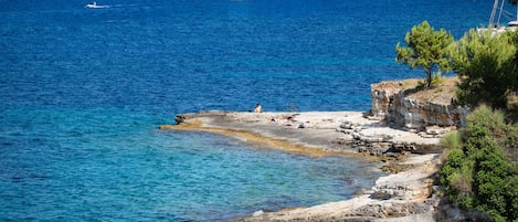 Eine Küstenlandschaft mit klarem, blauem Wasser, felsigen Klippen und einem Segelboot in der Ferne.