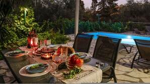 An outdoor dining area with a pool in the background, surrounded by greenery. - Villa Sevi in Loggos (Paxi)
