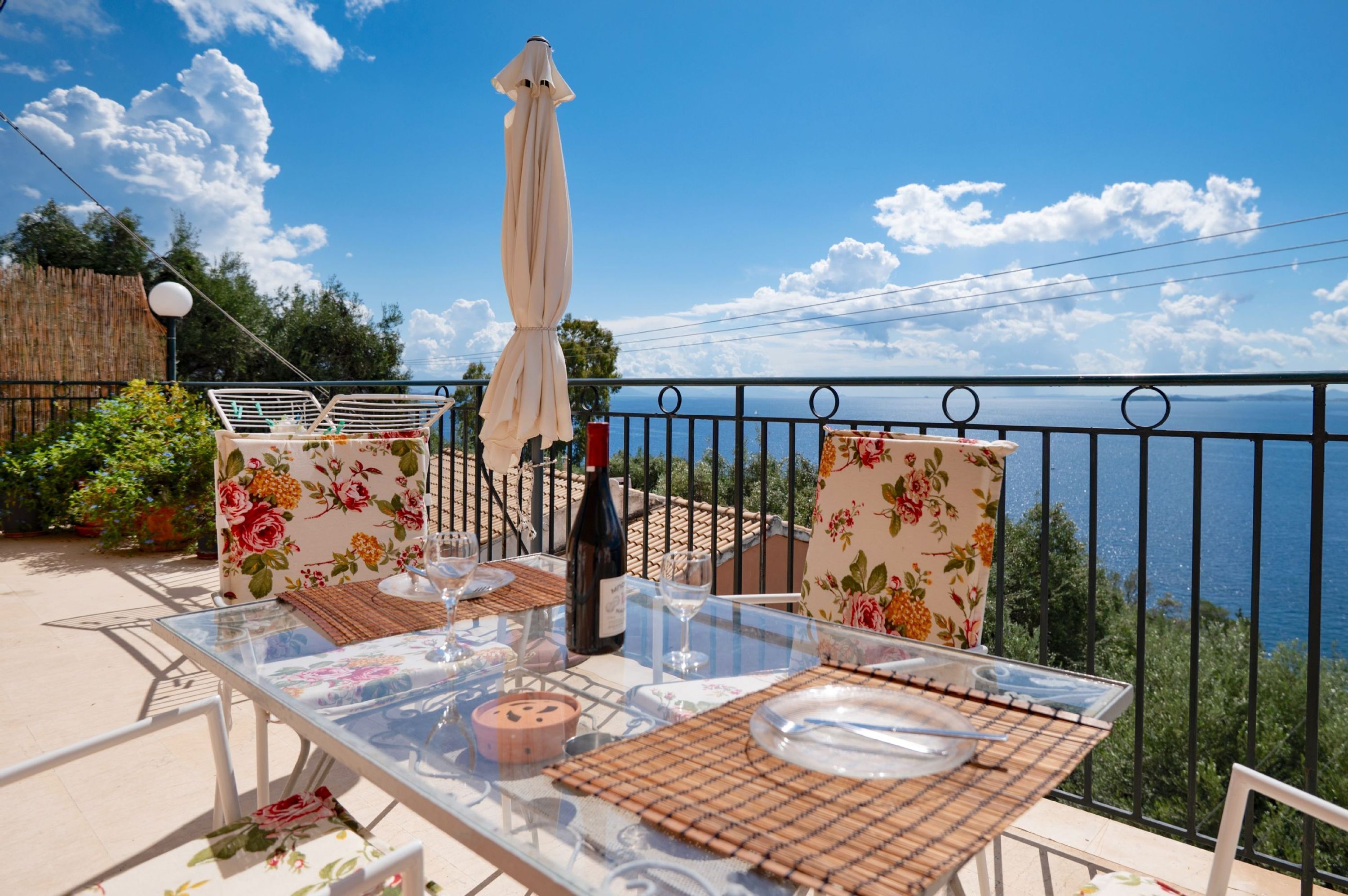 Ein Tisch draußen mit Meerblick, eine Weinflasche und stuhlähnliche Sitzgelegenheiten mit Blumenmuster.
