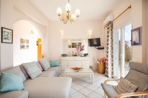 Ein modernes Wohnzimmer mit Sofa, Sessel, Couchtisch und Wand-Fernseher.
