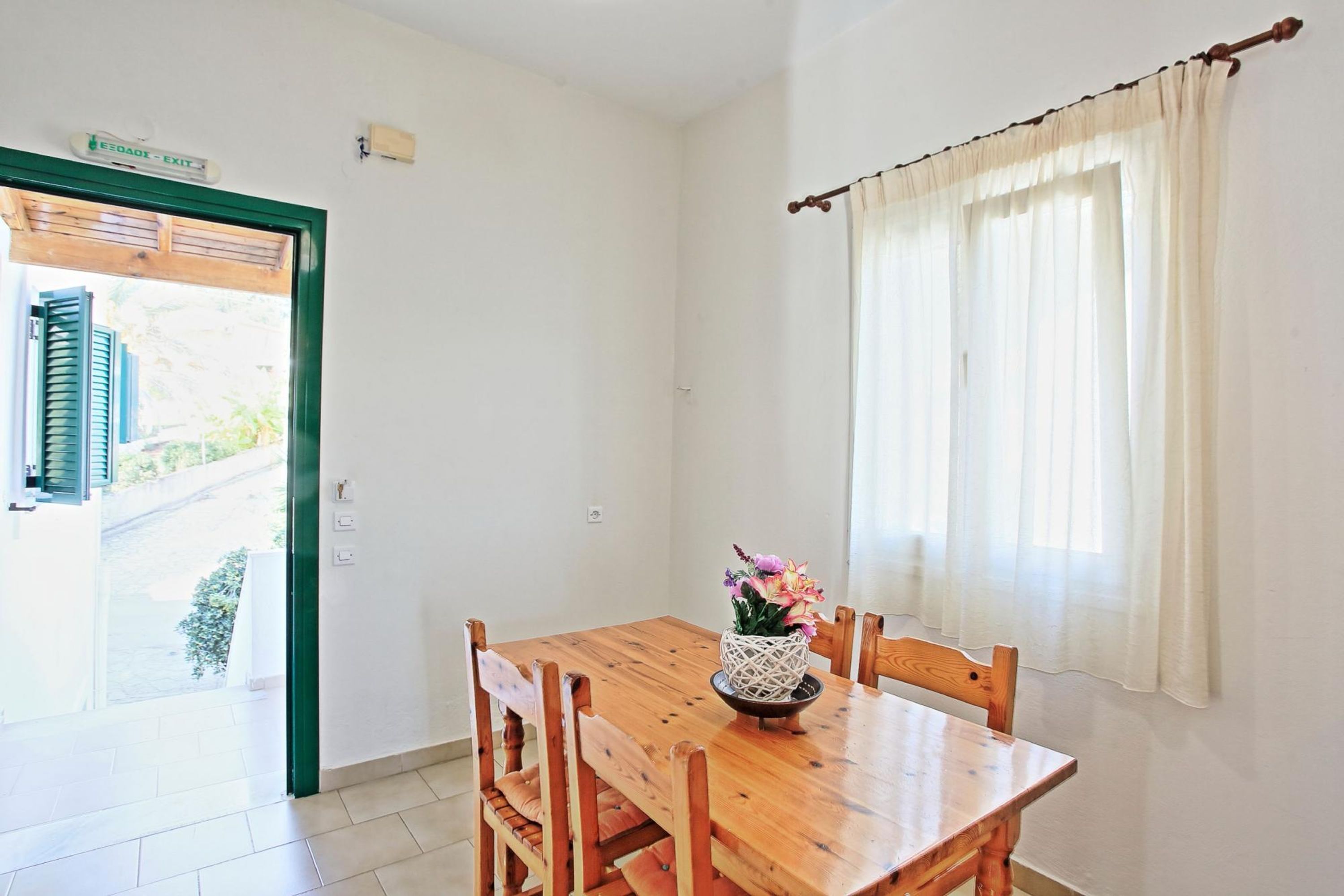 Comedor con mesa y sillas de madera, un florero con flores y una ventana con cortinas.