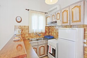 Eine Küche mit Holzausstattung, einem weißen Kühlschrank, einem Herd, einem Spülbecken und einer Wanduhr.