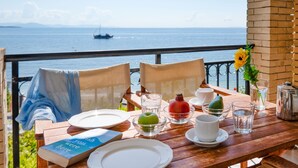 A wooden table set with plates, glasses, a book, and a pomegranate, overlooking a body of water. - Chrissa in Katavolos (Katavolos)