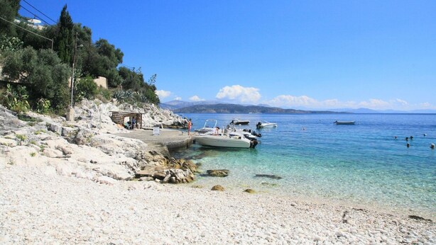 A pebble beach with boats docked, a small building, and clear blue water. - Chrissa in Katavolos (Katavolos)