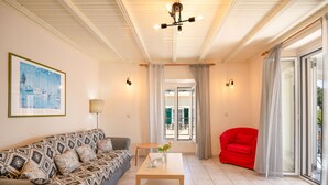 A living room with a patterned sofa, a wooden coffee table, a red armchair, and a large window with curtains. - Chrissa in Katavolos (Katavolos)