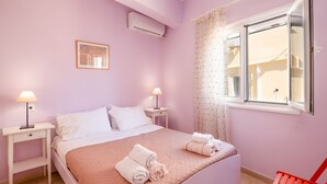 A bedroom with a bed, two bedside tables with lamps, a window with a view, and a wall-mounted air conditioner. - Chrissa in Katavolos (Katavolos)