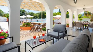 A covered outdoor seating area with a pool view, featuring a sofa, chairs, and tables. - Villa Paradiso in Agnos (Roda)