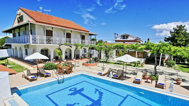 A pool with a geometric pattern, a two-story building with a balcony, and outdoor seating with umbrellas. - Villa Paradiso in Agnos (Roda)