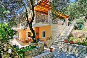 Ein zweistöckiges Haus mit Balkon, Außenbereich zum Sitzen und Blumentöpfen.