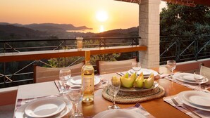 A dining table set for two with a bottle of wine, plates, and a basket of melon. - Sunset House in Sidari (Corfu)