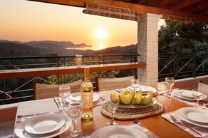 A dining table set for two with a bottle of wine, plates, and a basket of melon. - Sunset House in Sidari (Corfu)