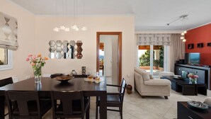 A modern living room with a sofa, TV, and a dining area with a table and chairs. - Sunset House in Sidari (Corfu)