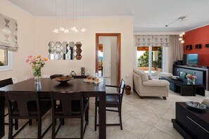 A modern living room with a sofa, TV, and a dining area with a table and chairs. - Sunset House in Sidari (Corfu)