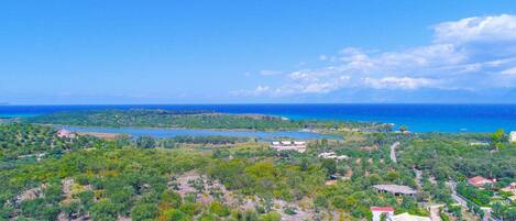 An aerial view of a coastal area with scattered buildings, a lake, and a clear blue sky.