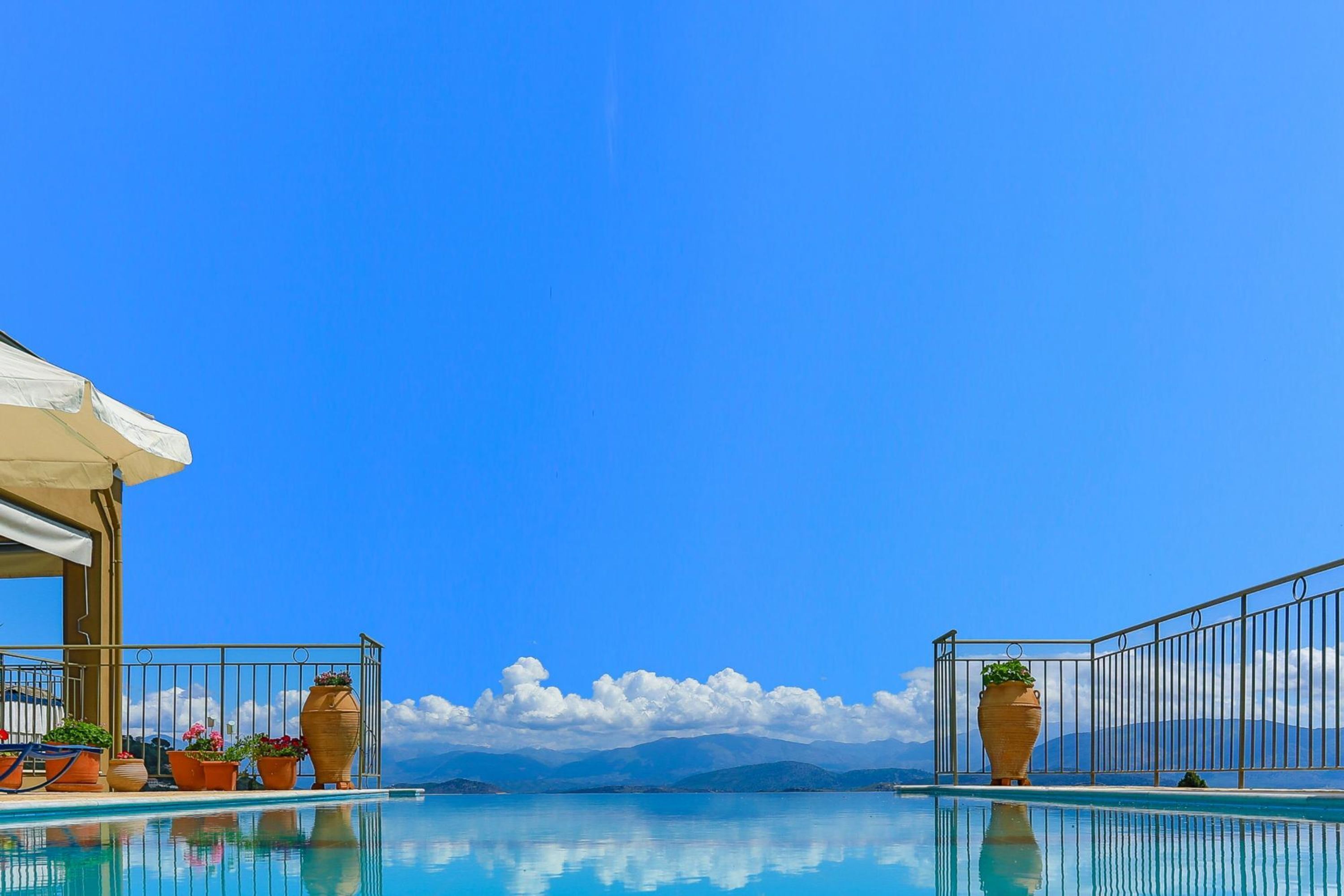 Céu azul claro, piscina com vista para montanhas e plantas em vasos na beira da piscina.