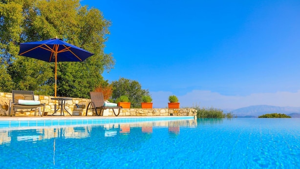 A clear blue pool with lounge chairs and an umbrella, surrounded by stone walls and potted plants. - Villa Helona in Lithiasmenos (Lithiasmenos)