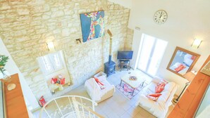 A spacious living area with a stone wall, a fireplace, a television, and a cozy seating arrangement. - Villa Helona in Lithiasmenos (Lithiasmenos)